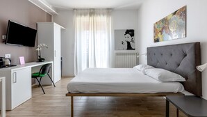 A modern hotel room with a bed, a desk with a computer, a TV, and a painting on the wall. - Cineteca Grey Studio I by Wonderful Italy (Bologna)