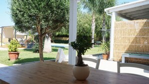 An outdoor patio with a wooden table, potted plants, and a white fence. - Dependance in Villa con Piscina by Wonderful Italy (Syracuse)