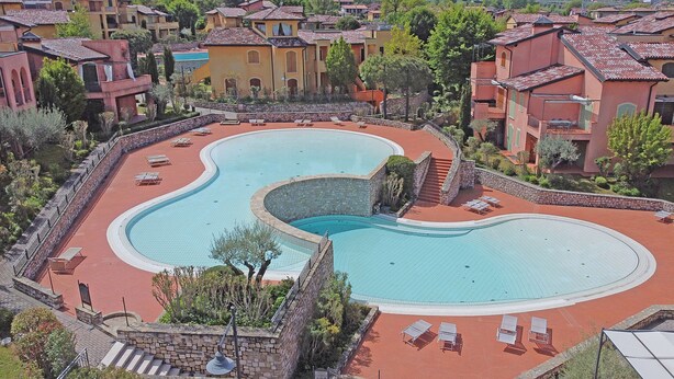 A large, kidney-shaped swimming pool surrounded by lounge chairs and a stone wall. - Borgo del Torchio A14 con Piscina by Wonderful Italy (Manerba del Garda)