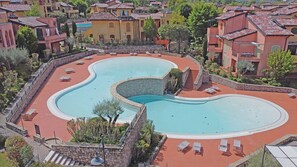 Una piscina grande con forma de riñón, rodeada de sillas de descanso y un muro de piedra.
