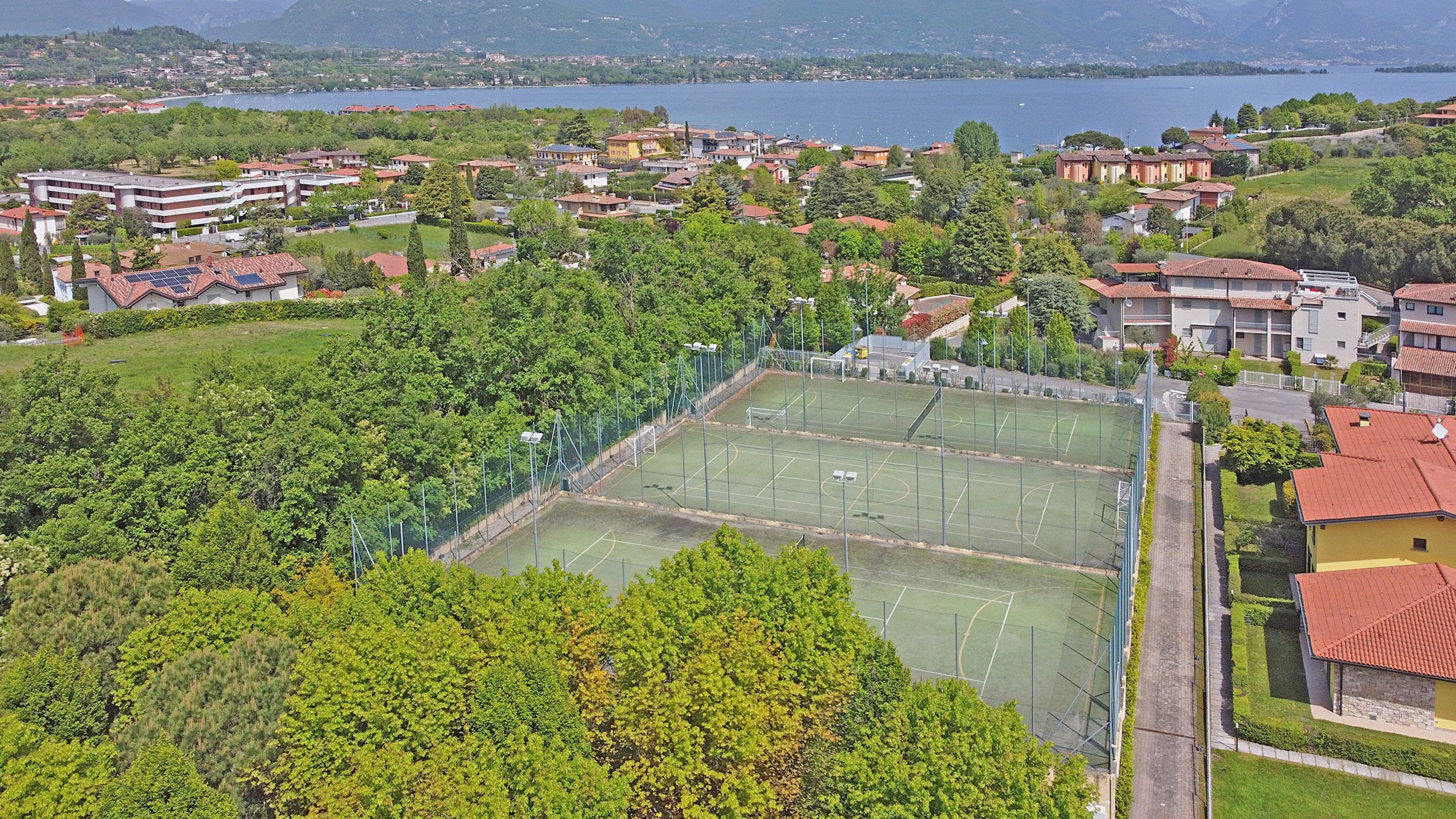 Ein Wohngebiet mit mehreren Gebäuden, einem Tennisplatz und einem See im Hintergrund.