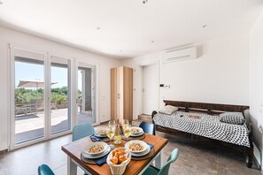 Un dormitorio moderno con cama, un área de comedor con mesa para dos personas y un balcón con mobiliario exterior.