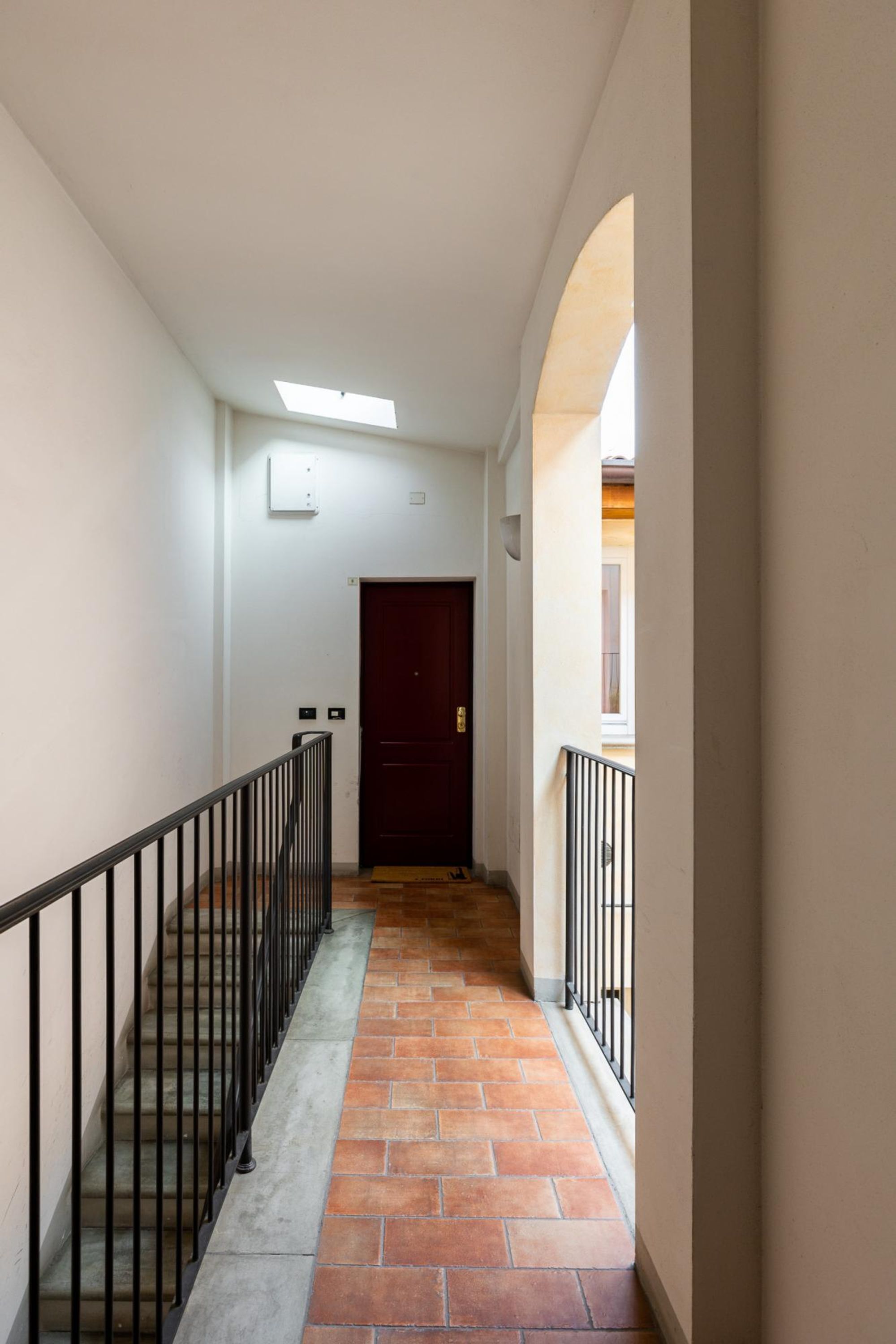 A narrow hallway with a tiled floor, a dark door at the end, and a small window on the left.