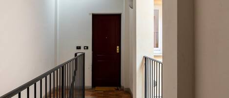 A narrow hallway with a tiled floor, a dark door at the end, and a small window on the left.