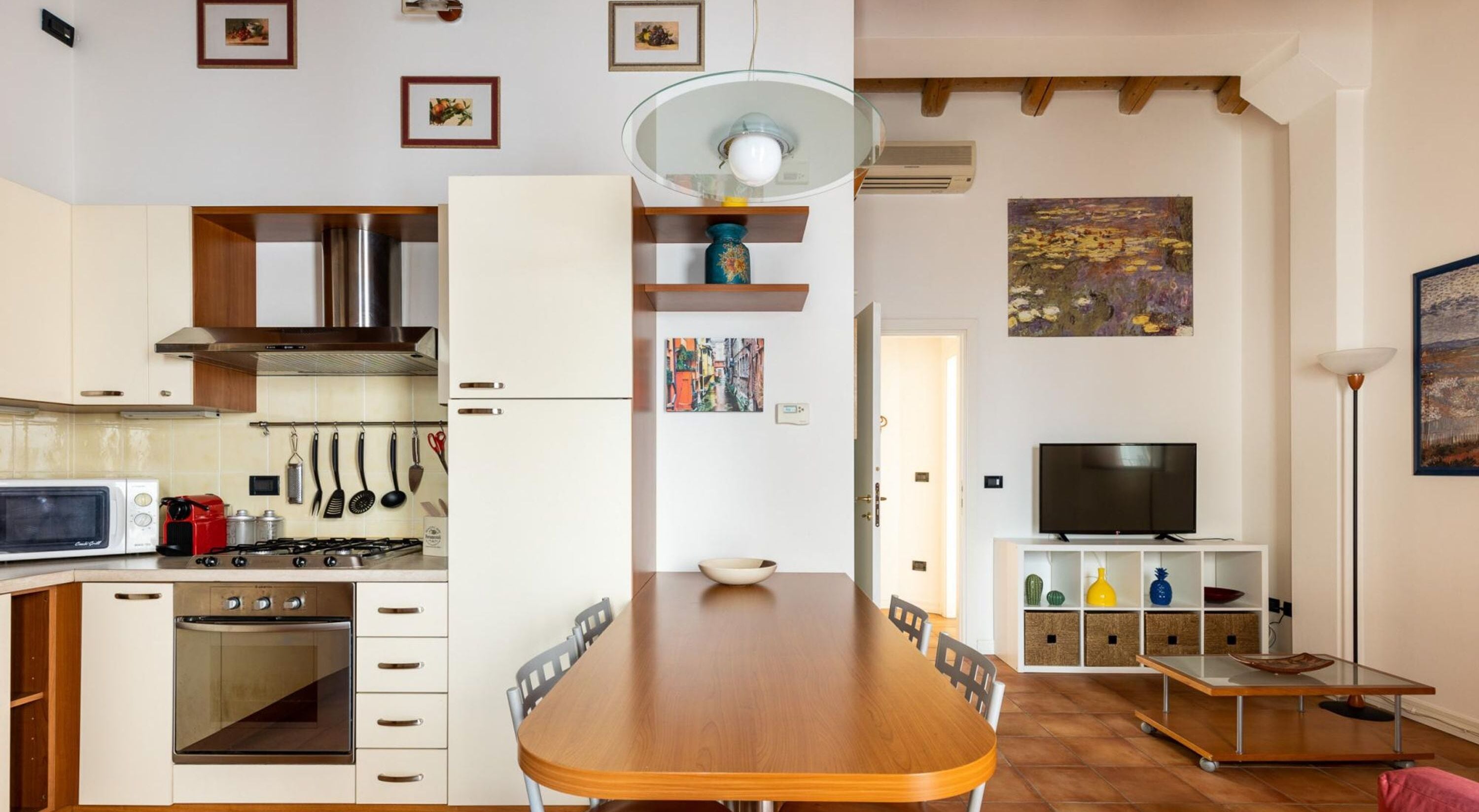 Une cuisine compacte dotée d’appareils électroménagers modernes, un coin repas avec une table en bois et un téléviseur posé sur un meuble blanc.