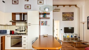 Eine kompakte Küche mit modernen Geräten, ein Essbereich mit Holztisch und ein Fernseher auf einem weißen Schrank.