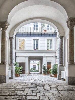 Un couloir en arc de cercle, doté d’un sol en pierre, de colonnes et de plantes en pot.