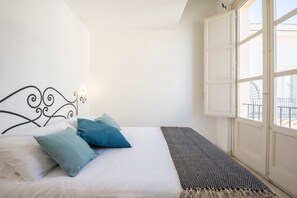 A bedroom with a bed, pillows, a bedside table, a window with a view, and a door.