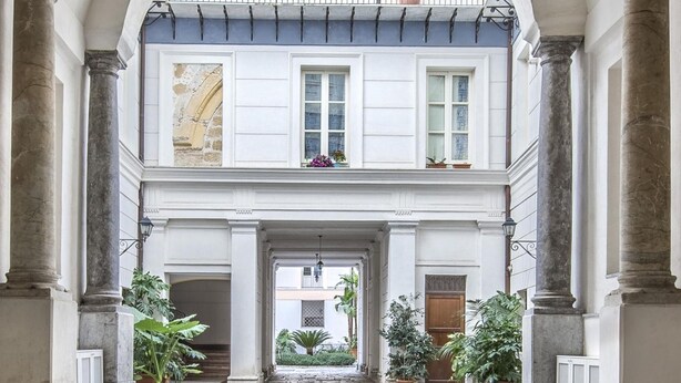 Un patio con suelo de piedra, arcos, columnas y plantas en macetas.