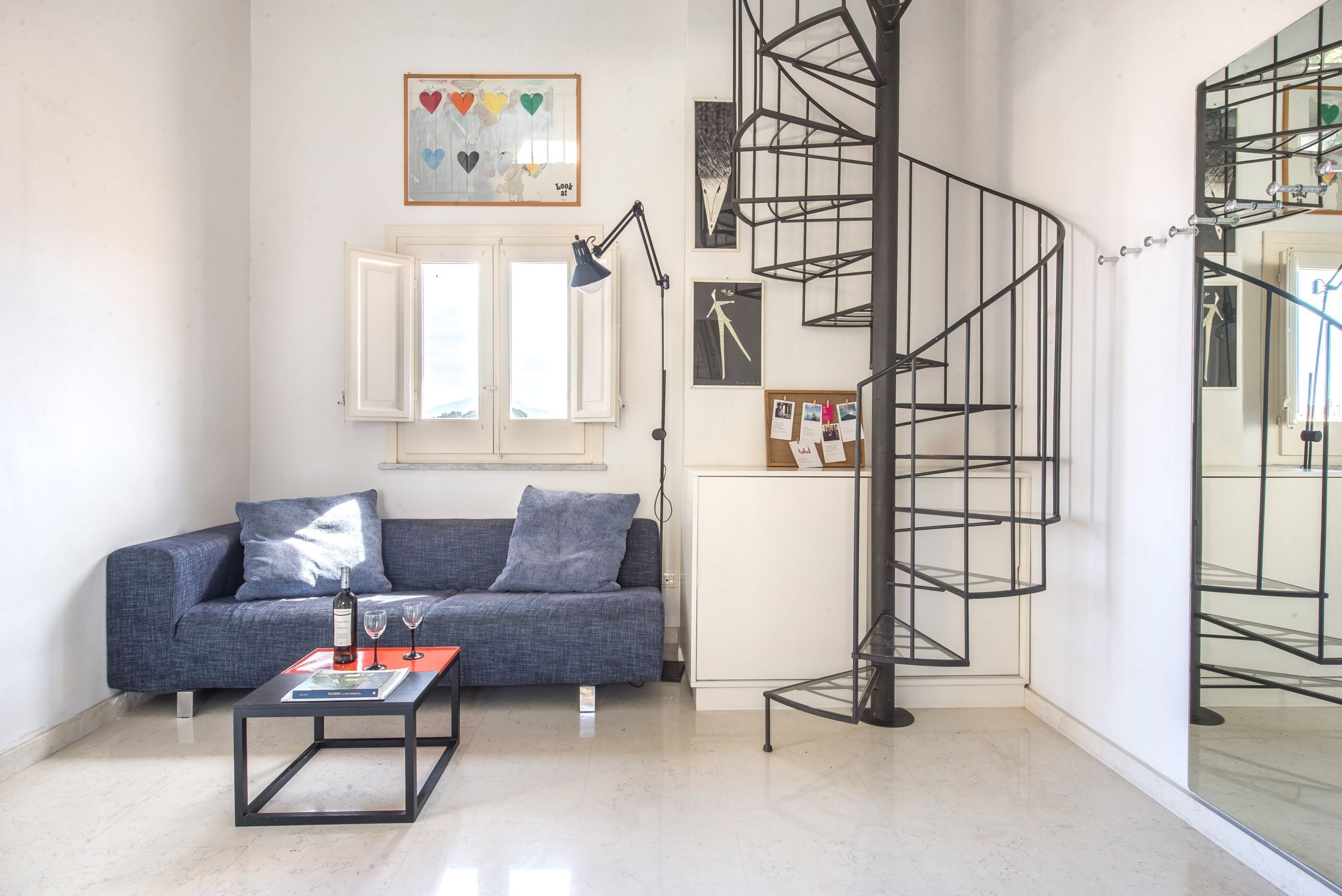 A modern living room with a blue sofa, a coffee table, a spiral staircase, and a wall-mounted artwork.
