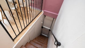 Una escalera con peldaños de madera y barandillas negras que conduce a una habitación con paredes blancas y una pared de acento rosa.