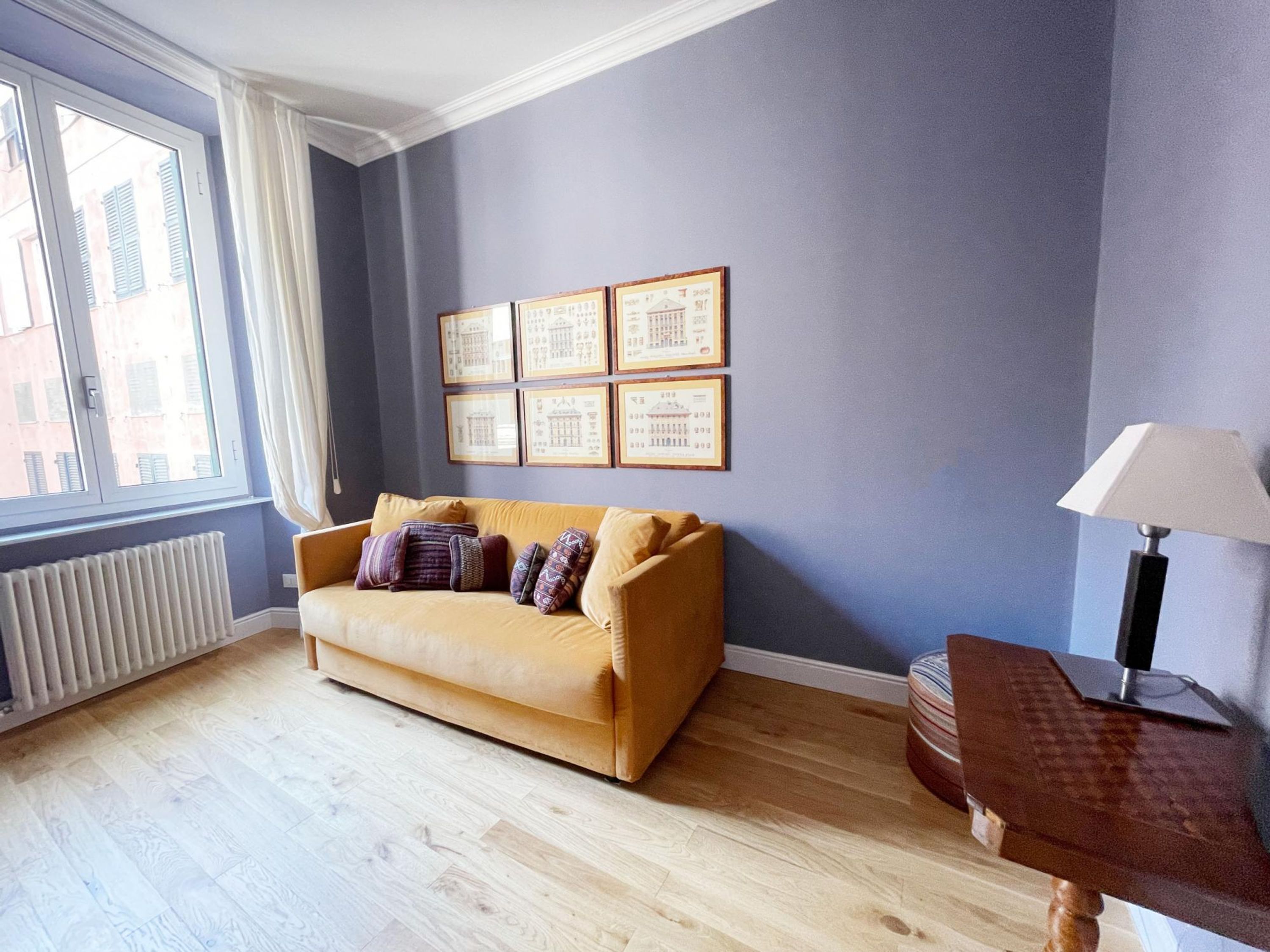 A room with a sofa, framed pictures on the wall, a lamp, and a radiator.