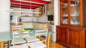 Eine kleine Küche mit einem Glastisch, weißen Stühlen, einem Holzkasten und einer rot-weiß gestreiften Decke.