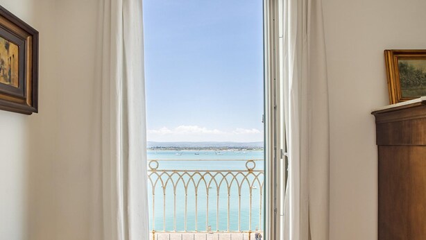 Eine offene Tür, die auf einen Balkon mit Blick auf das Meer und das entfernte Land führt.
