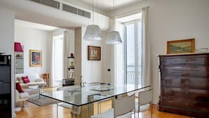 Ein modernes Wohnzimmer mit einem Glastisch, weißen Stühlen und einer Holzkommode.