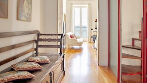 Ein Flur mit einer Holzbank, einem weißen Sessel und einer Treppe mit roten Geländern.