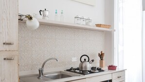 Eine moderne Küche mit weiß gefliestem Fliesenspiegel, Spüle aus Edelstahl und Gaskochfeld. Unter der Arbeitsplatte befinden sich Schränke und zur Rechten ein Fenster.