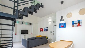 A modern living room with a grey sofa, a wooden coffee table, a TV, and a staircase.