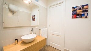 A bathroom with a white sink, wooden vanity, and a large mirror. There is a door with a poster on the wall.