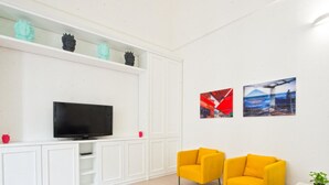 A modern living room with a flat-screen TV, two yellow armchairs, and two framed pictures on the wall.