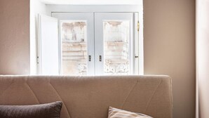 A beige sofa with two pillows, a white door with glass panels, and a view of a stone balustrade.
