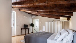 A bedroom with a wooden ceiling, a bed with white bedding, a bedside table with a lamp, and a TV on a stand.