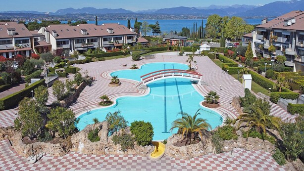 A resort with a central swimming pool, landscaped gardens, and mountain views. - I Ciliegi 1-09 con Piscina by Wonderful Italy (Desenzano del Garda)