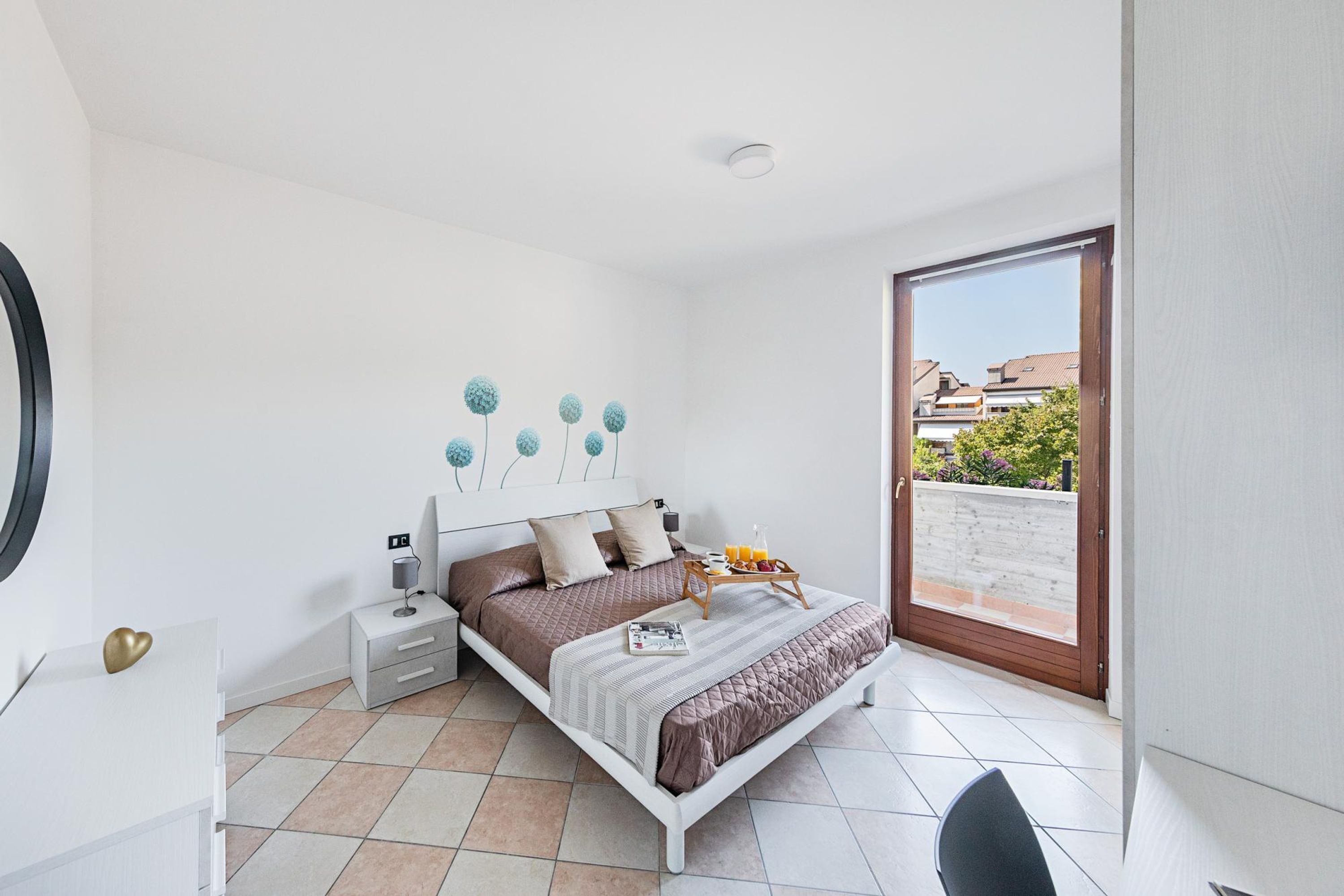 A bedroom with a bed, bedside tables, a chair, and a view of the outside.