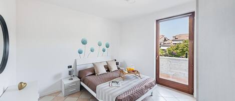 A bedroom with a bed, bedside tables, a chair, and a view of the outside.