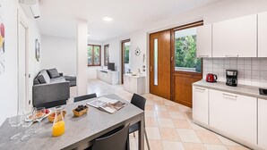 A modern kitchen with white cabinets, a dining area with a grey table and chairs, and a living area with a grey sofa. - I Ciliegi 1-09 con Piscina by Wonderful Italy (Desenzano del Garda)