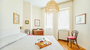 Een netjes ingerichte slaapkamer met een groot bed, een houten dressoir, een stoel en een raam met gordijnen.