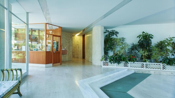 Een moderne lobby met een receptiebalie, een zithoek en binnenshuis planten.