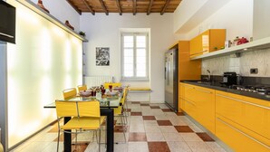 A kitchen with yellow cabinets, a stainless steel refrigerator, and a dining area with yellow chairs and a glass table.