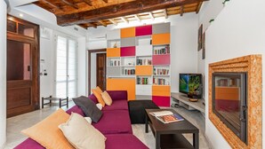 A living room with a wooden ceiling, a sofa set, a bookshelf, and a television.