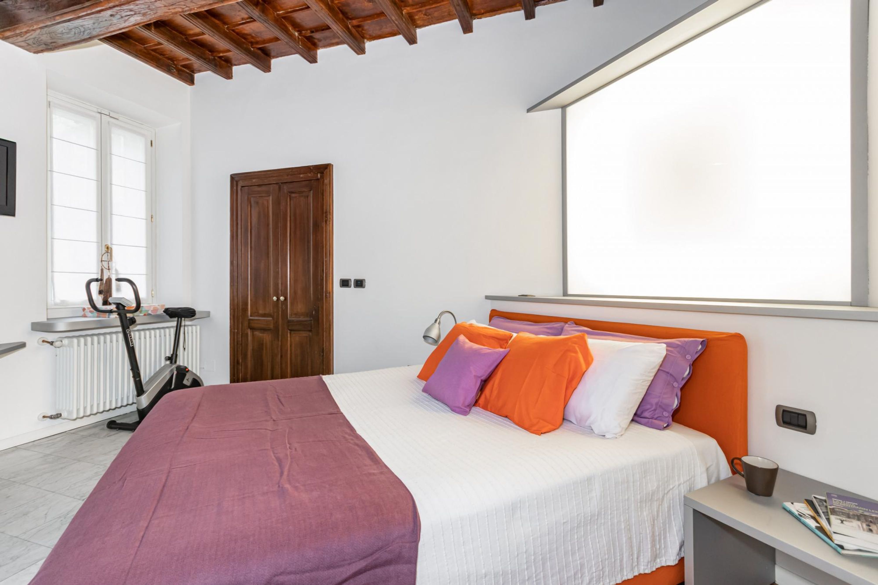 A bedroom with a bed, a window, a door, and an exercise bike.