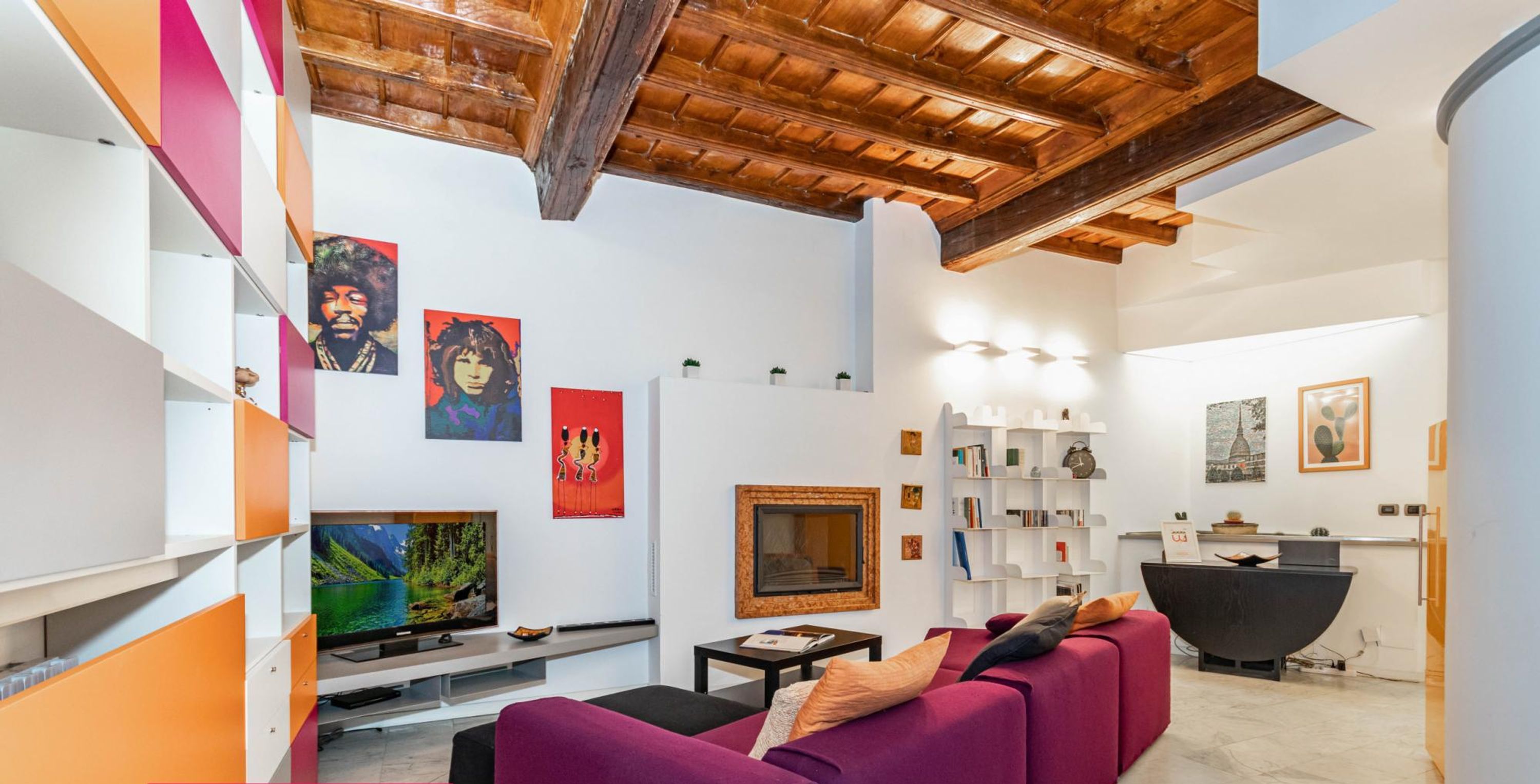 Un salon moderne avec un canapé violet, un téléviseur à écran plat et des œuvres d’art accrochées aux murs.