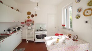 A kitchen with white cabinets, a stove, a microwave, and a dining table set with plates and cups. - Villa Flores a Mondello by Wonderful Italy (Palermo)