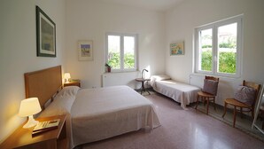 A hotel room with two beds, a desk with a lamp, a chair, and two windows providing views of greenery. - Villa Flores a Mondello by Wonderful Italy (Palermo)
