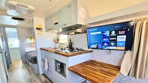 Una cocina compacta con estufa integrada, encimera de madera y televisor de pantalla plana montado en la pared.