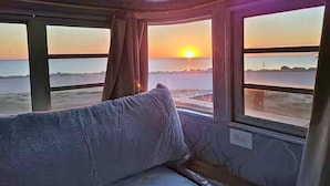 Una habitación con cama, ventana y vista al atardecer sobre el agua.
