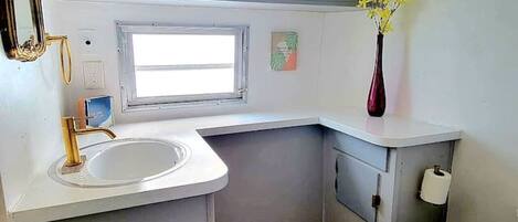 A compact kitchenette with a sink, a window, and a toilet.