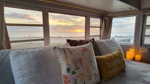 Una cama con almohadones florales y vistas al atardecer sobre el agua.