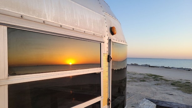 Un remolque con un ventanal grande que refleja una puesta de sol sobre el océano.
