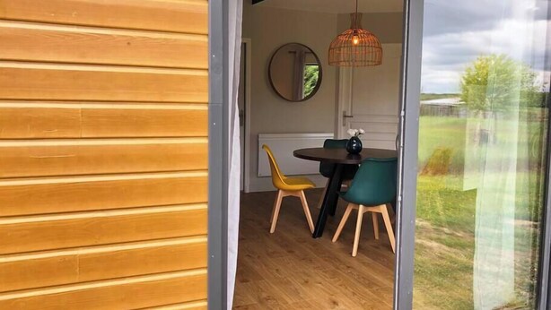 A dining area with a wooden table and chairs, a hanging light fixture, and a view of the outdoors through a glass door. - Gites-domainedupin, cottage "Mosnes à Lisa" (Mosnes)