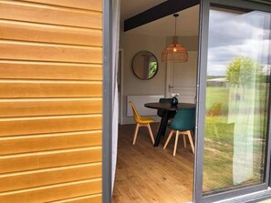 Un coin repas avec une table et des chaises en bois, un luminaire suspendu et une vue sur l’extérieur grâce à une porte vitrée.