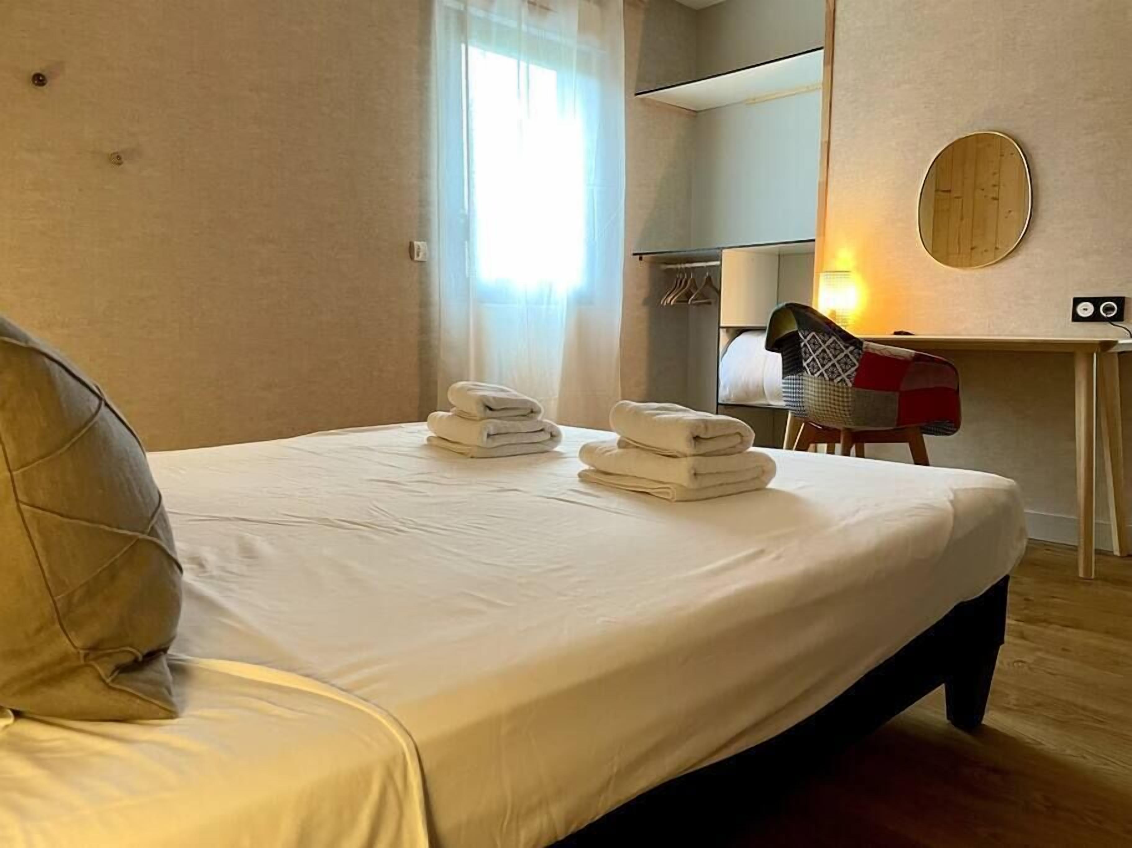 Habitación de hotel con cama, escritorio y silla. Hay toallas sobre la cama y una lámpara en el escritorio.