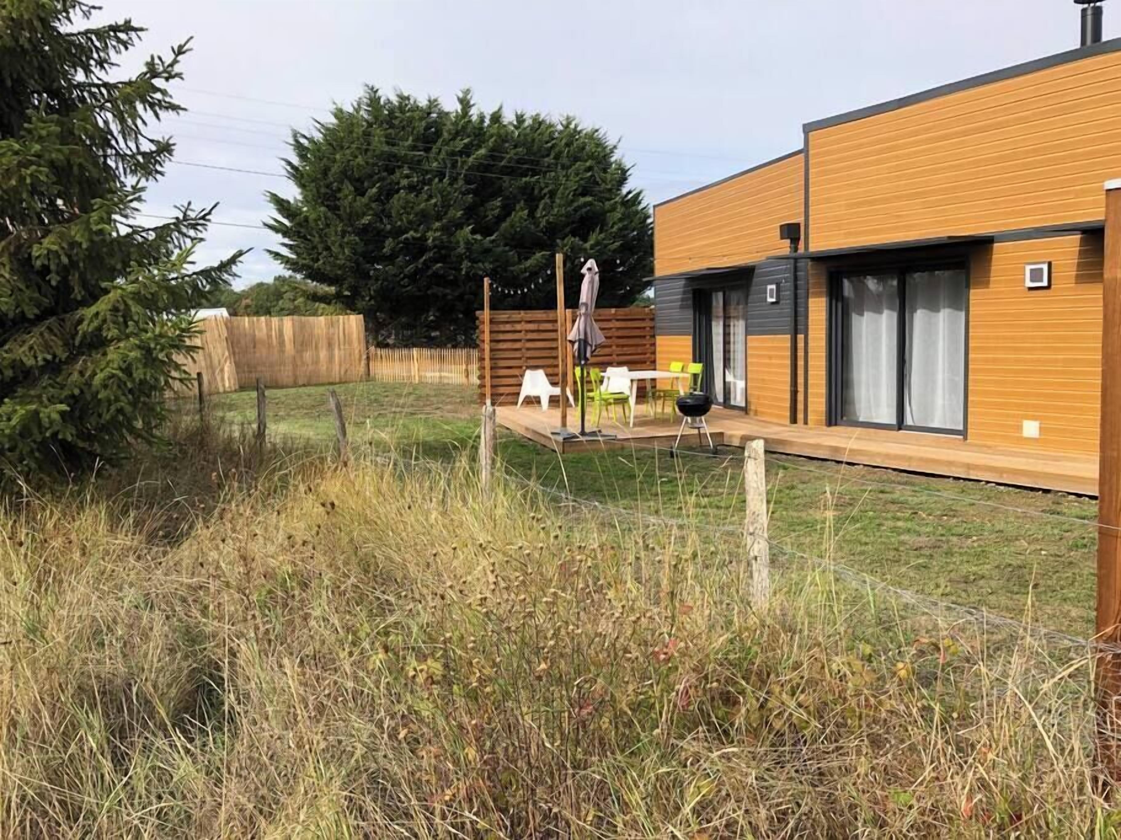 Una casa moderna de dos pisos con fachada de madera, patio trasero cercado y zona de estar al aire libre con mobiliario.