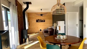 A modern living room with a wooden floor, a round dining table with yellow chairs, a black fireplace, and a hanging light fixture. - Gites-domainedupin, cottage "Mosnes à Lisa" (Mosnes)