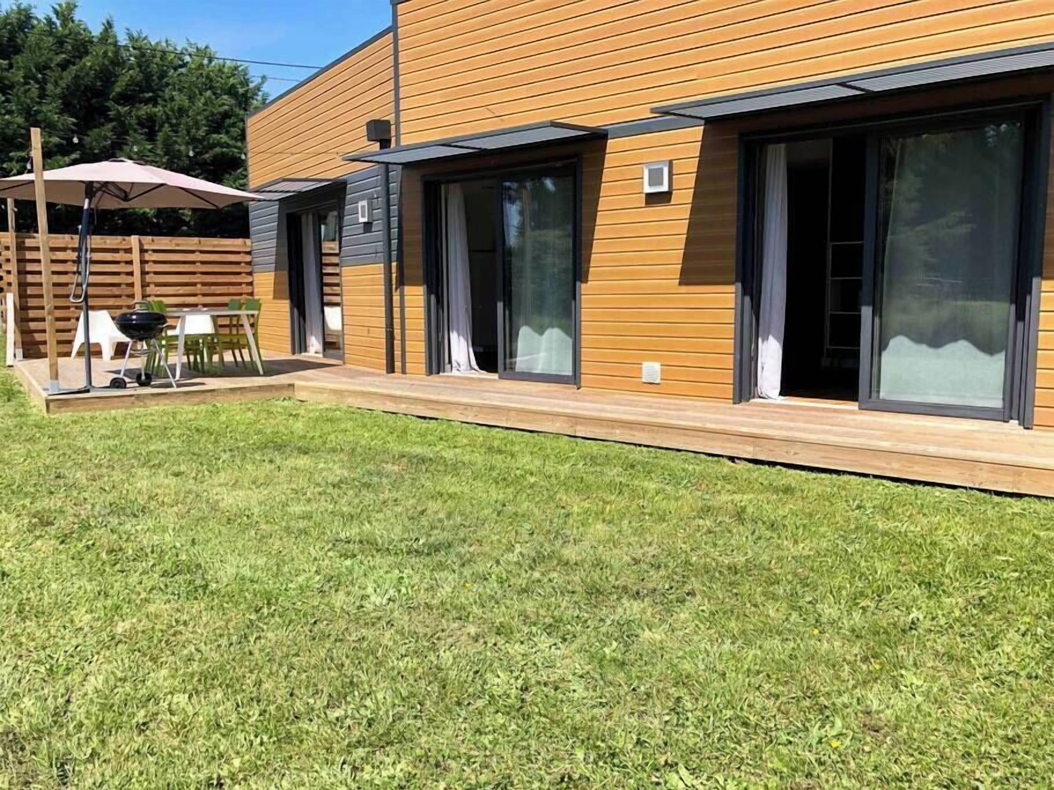 Ett modernt hus med stora skjutbara glasdörrar, ett trädäck och en uteplats med utemöbler.