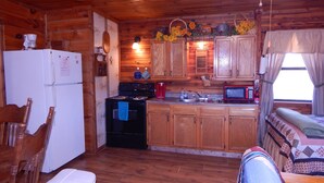 Une cuisine chaleureuse, aménagée dans le style d’un chalet, avec des meubles en bois, un réfrigérateur, une cuisinière et un four à micro-ondes.